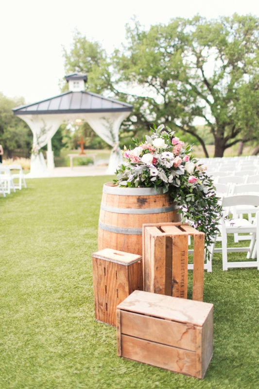 Wood barrels and crates and flowers used as wedding aisle decor.