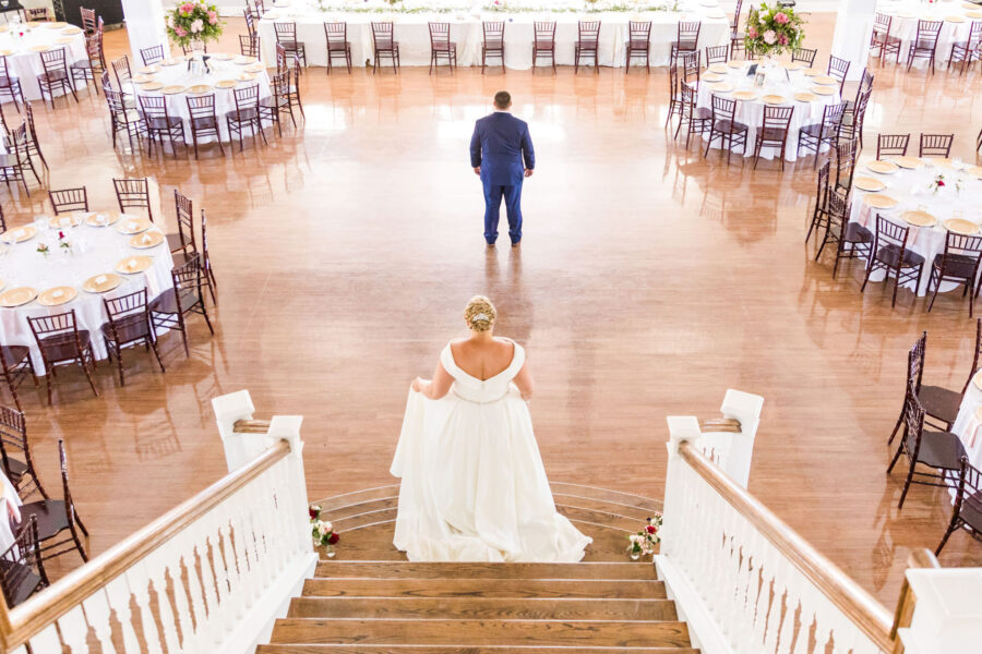 Bride walking down Kendall Point grand staircase to surprise her groom for the first look