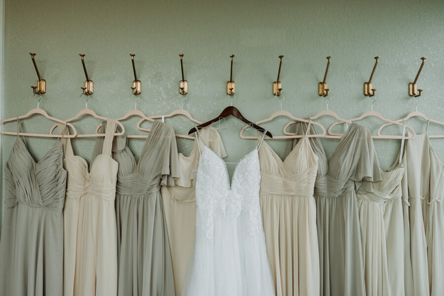 wedding gown and neutral bridesmaids dresses hanging on wall hooks