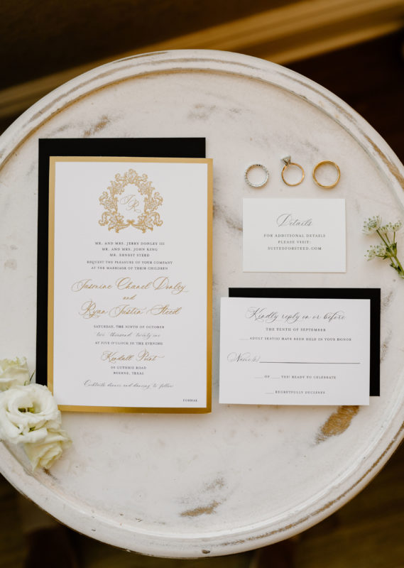 The wedding invitation and RSVP card arranged on a plate with the rings.