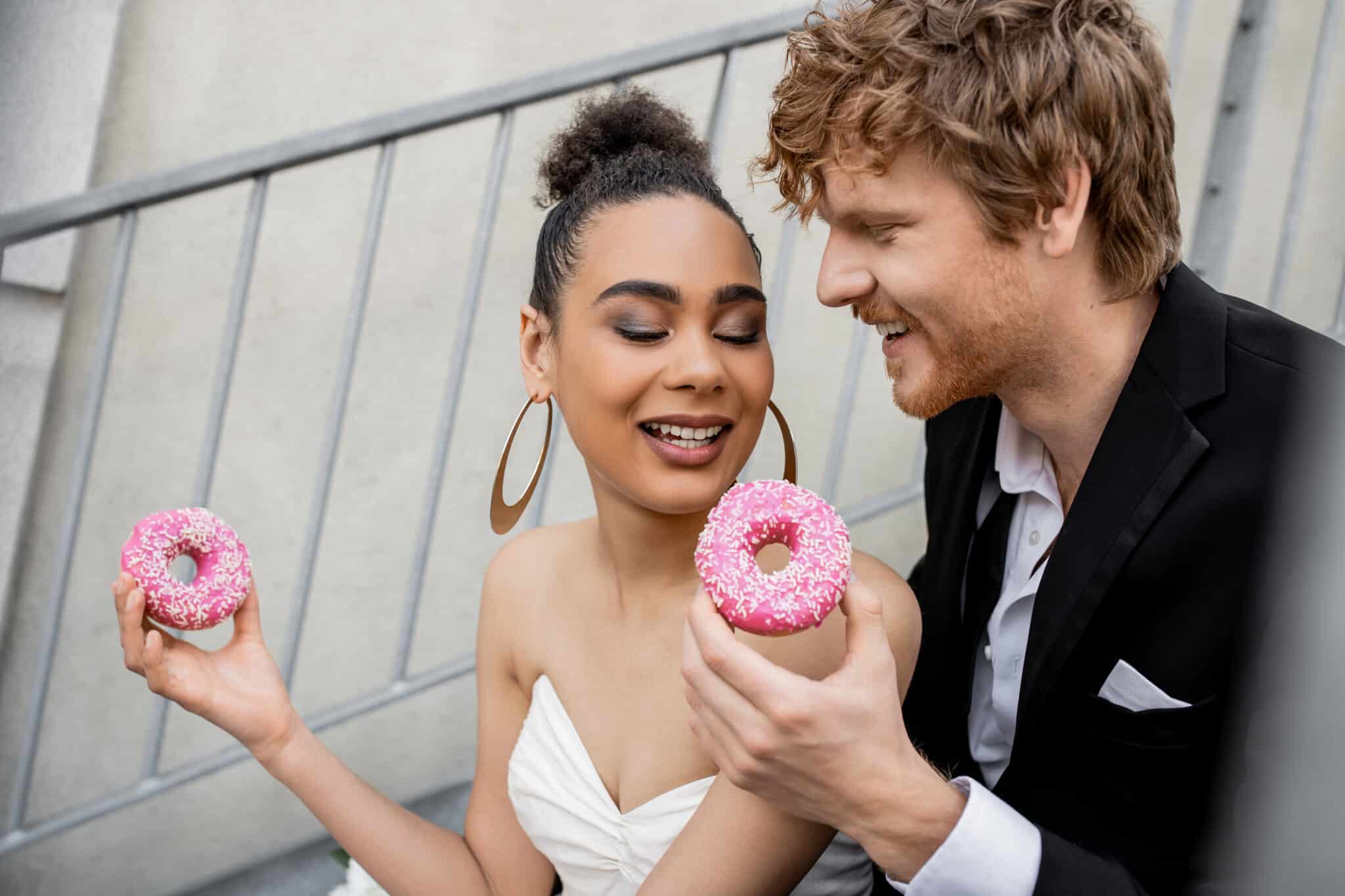 bride and groom holding pink donuts