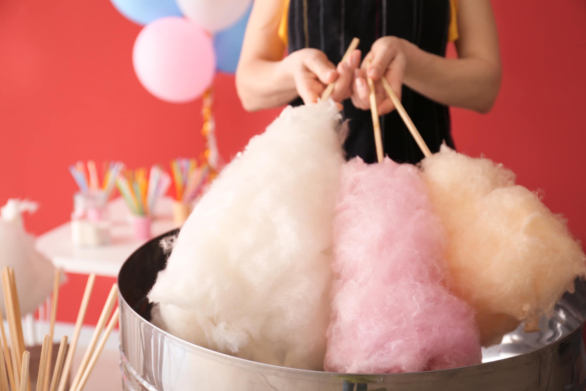 woman holding three sticks of cotton candy over machine