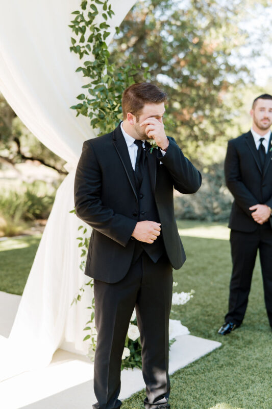 The groom wipes away a tear as he sees his bride walking down the aisle.