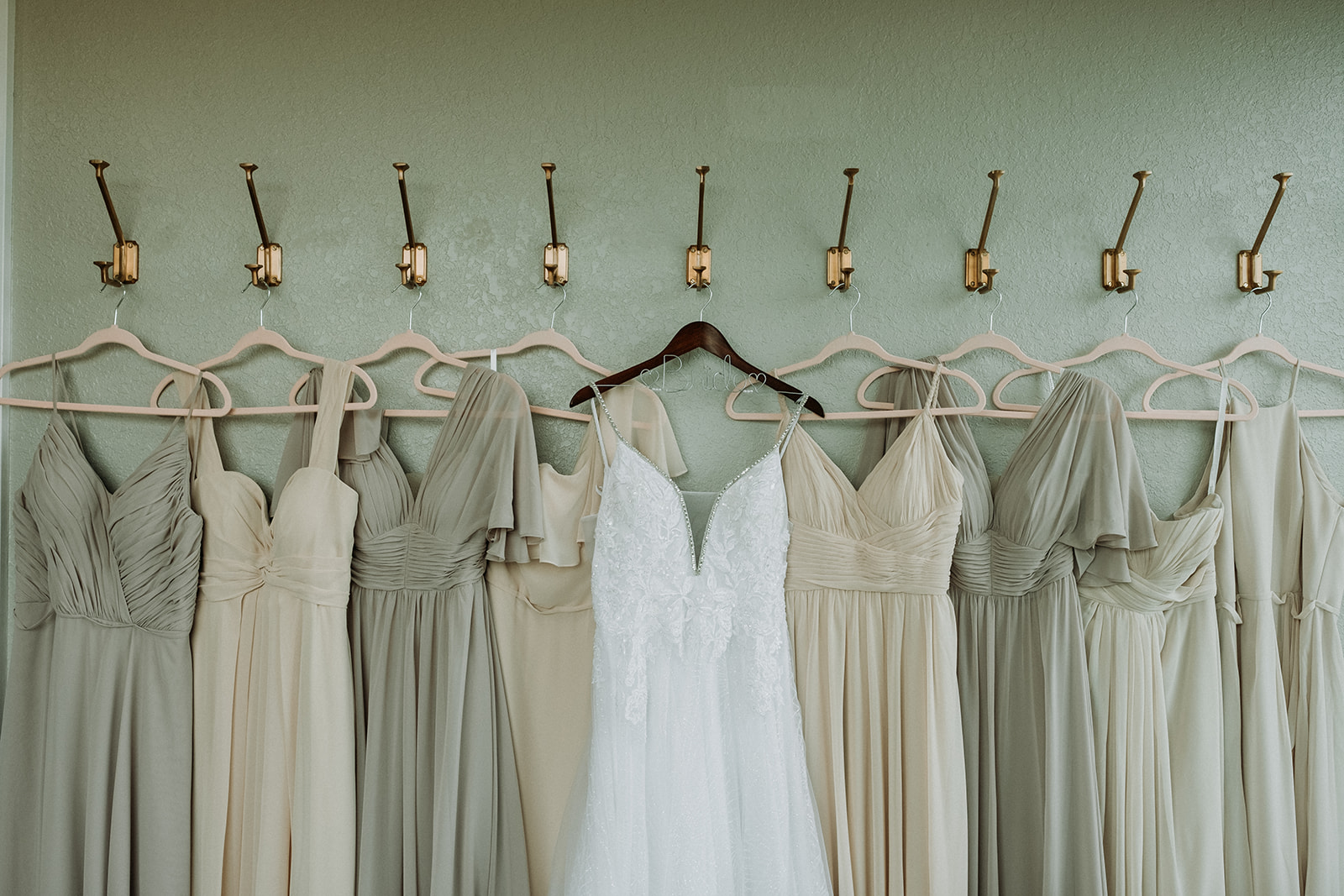 wedding gown and neutral bridesmaids dresses hanging on wall hooks