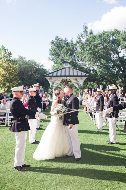 Bride and groom kiss as marines draw swords.