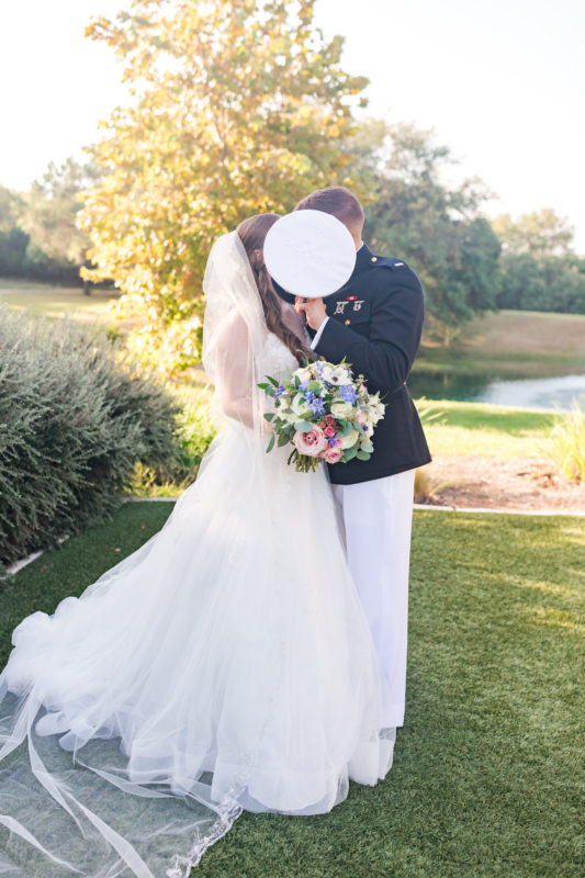 The groom holds his marine cap in front of him kissing his bride.