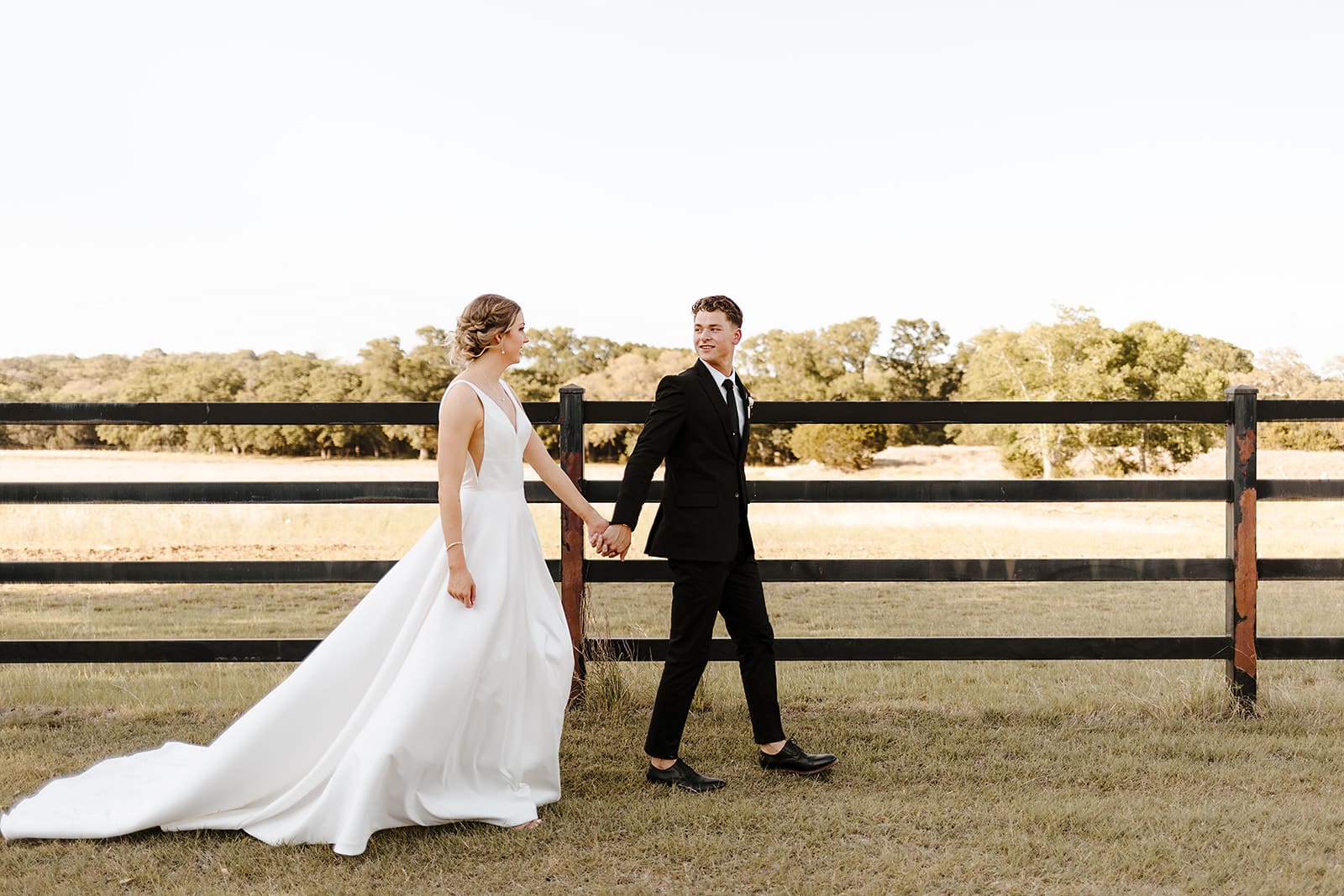 Bride and groom walking next to fence in pasture