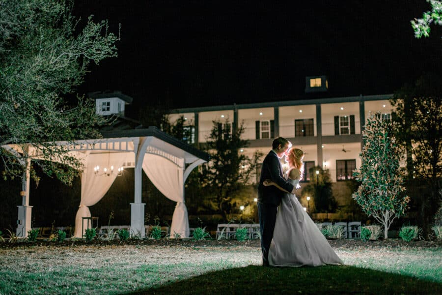 nighttime photo of bride and groom kissing with Kendall Point venue behind them