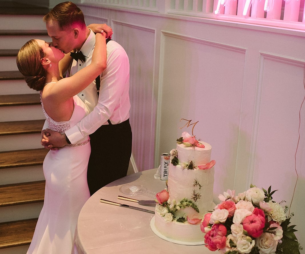 bride and groom kissing next to wedding cake
