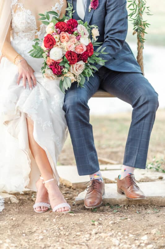 bride holding a cascading bouquet of roses and carnations while sitting on kendall point swing with groom