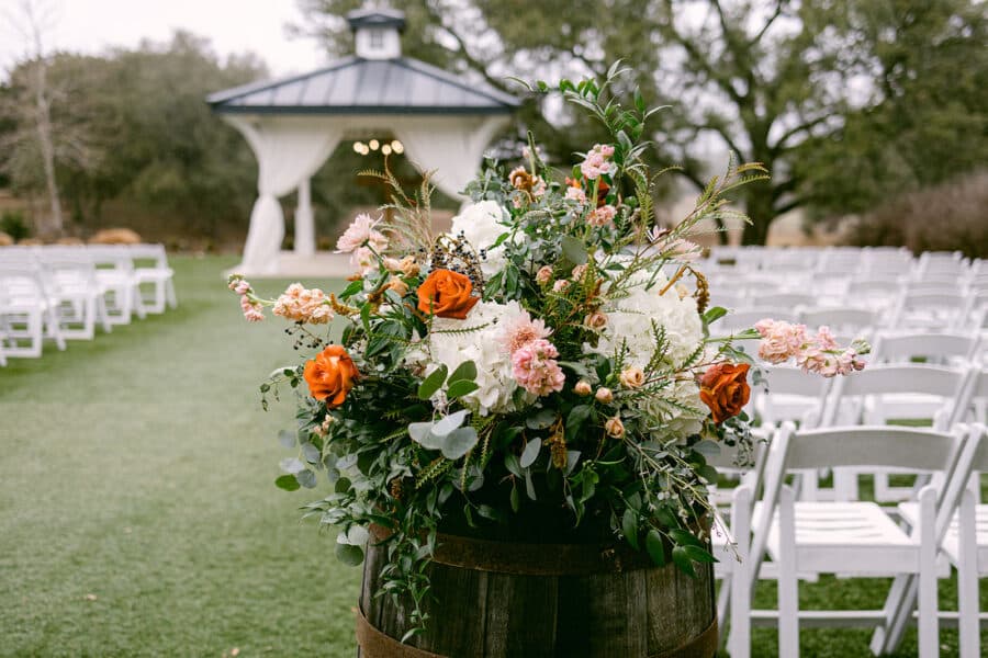 floral arrangement sitting atop wooden barrels lining the aisle at kendall point wedding