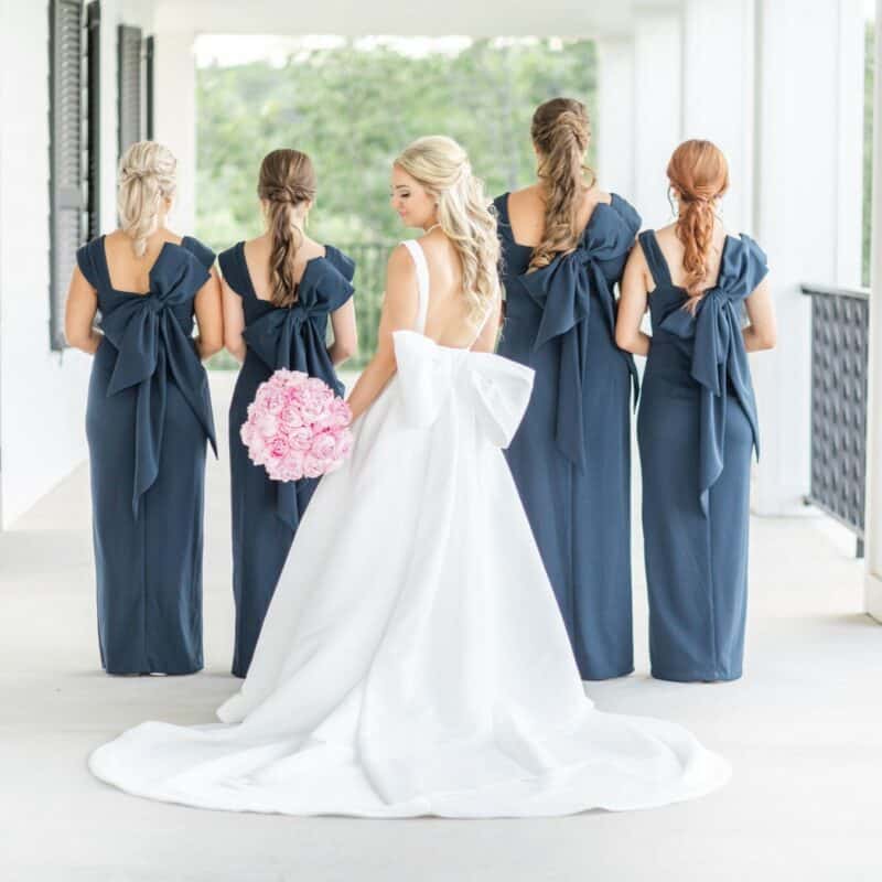 bride holding round bouquet of pink roses with her bridesmaids on kendall point terrace