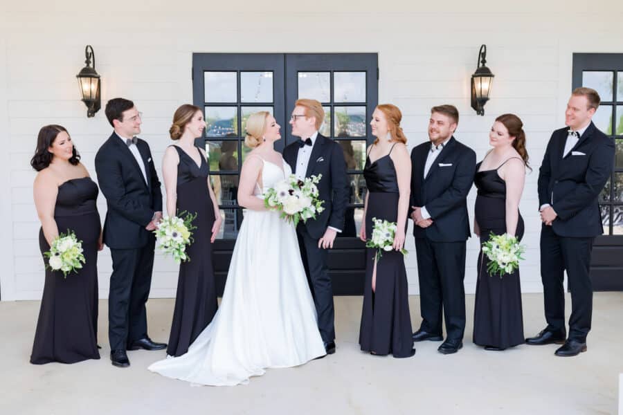 bride and groom look at each other while wedding party looks on standing on kendall point terrace