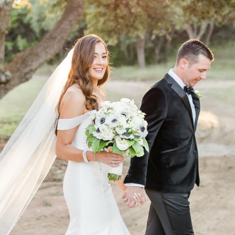 bride and groom walking kendall point grounds while bride holds bouquet of winter flowers