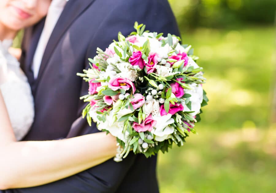 round wedding bouquet in bride's hand as she embraces groom