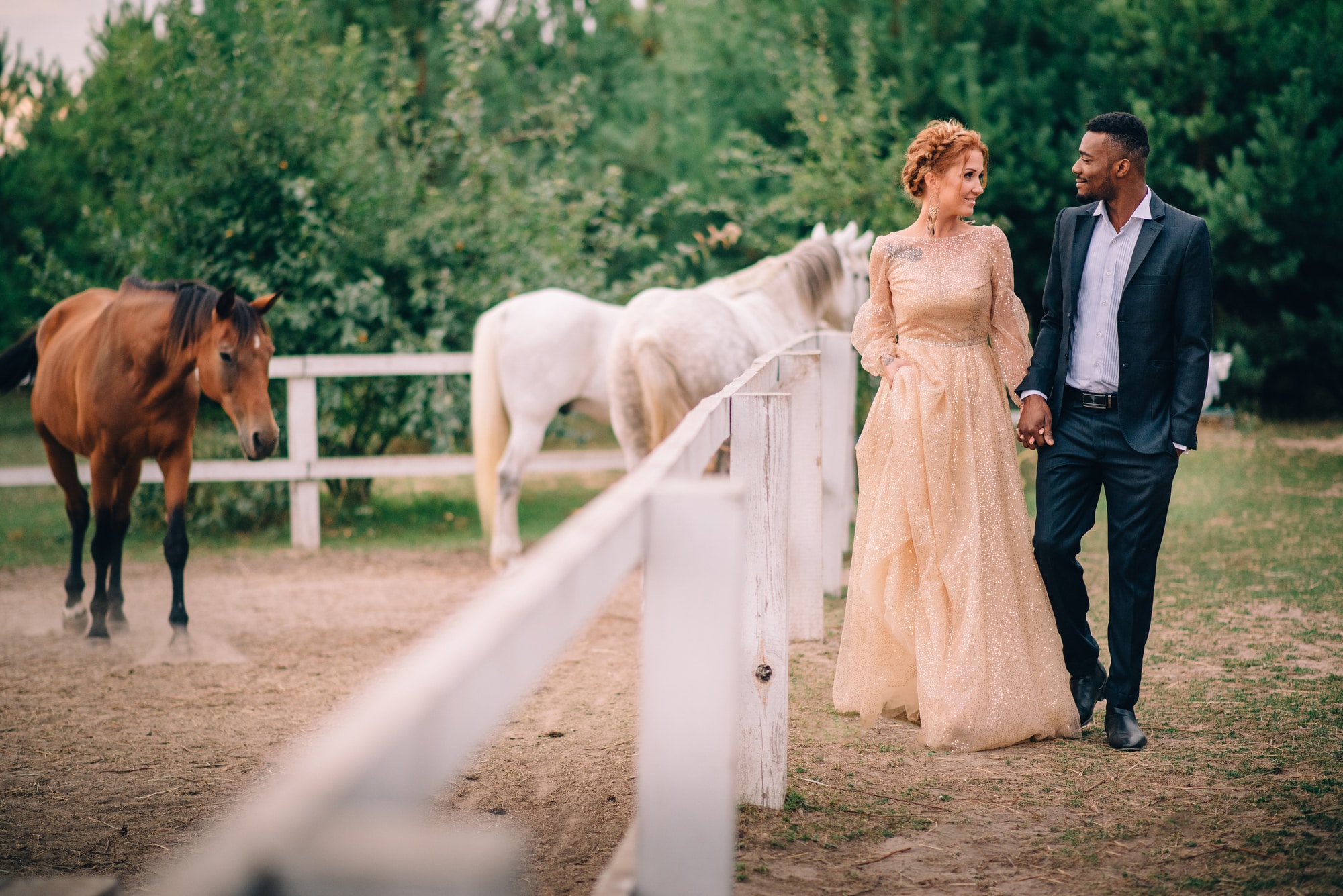 bride and groom walking next to horse corral